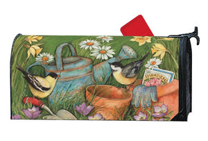 MailWrap with a goldfinch and chickadee sitting on garden tools next to a pair of garden gloves, pack of flower seeds, a watering can and two empty clay flower pots surrounded by wildflowers